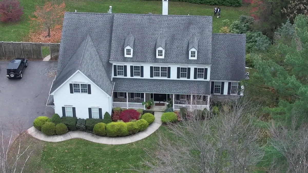 Oblique view of a two-story house, shingle roof, lawn and surrounding trees